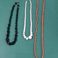 Três colares em tons de preto, branco e coral